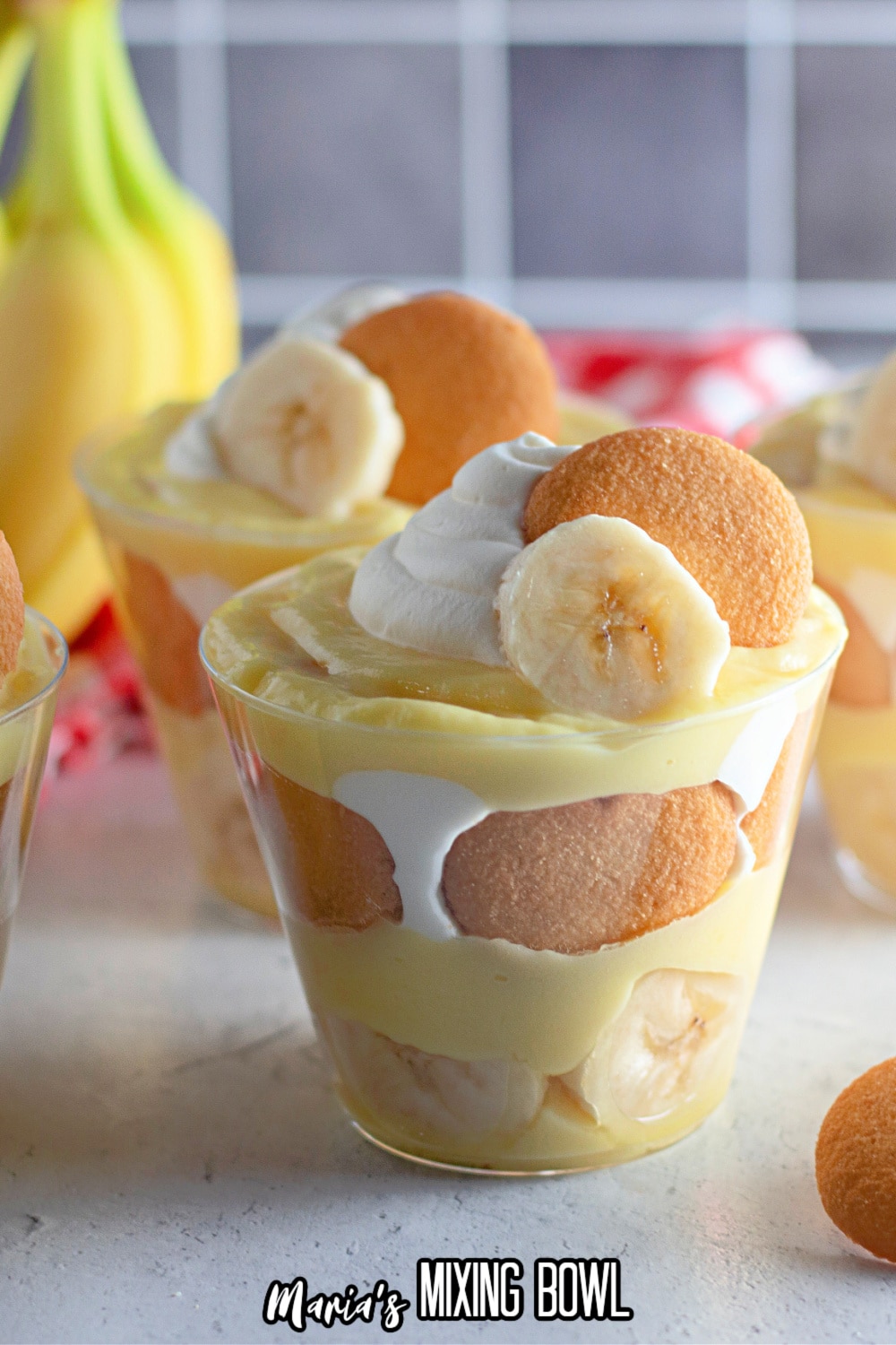 banana pudding in a clear plastic cup with a bunch of bananas in the background