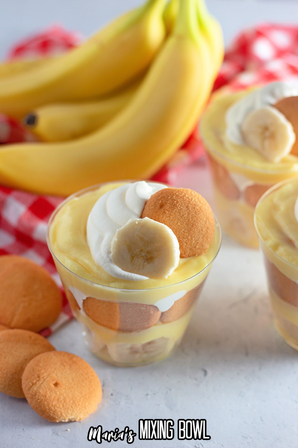 banana pudding in a clear plastic cup with a bunch of bananas in the background