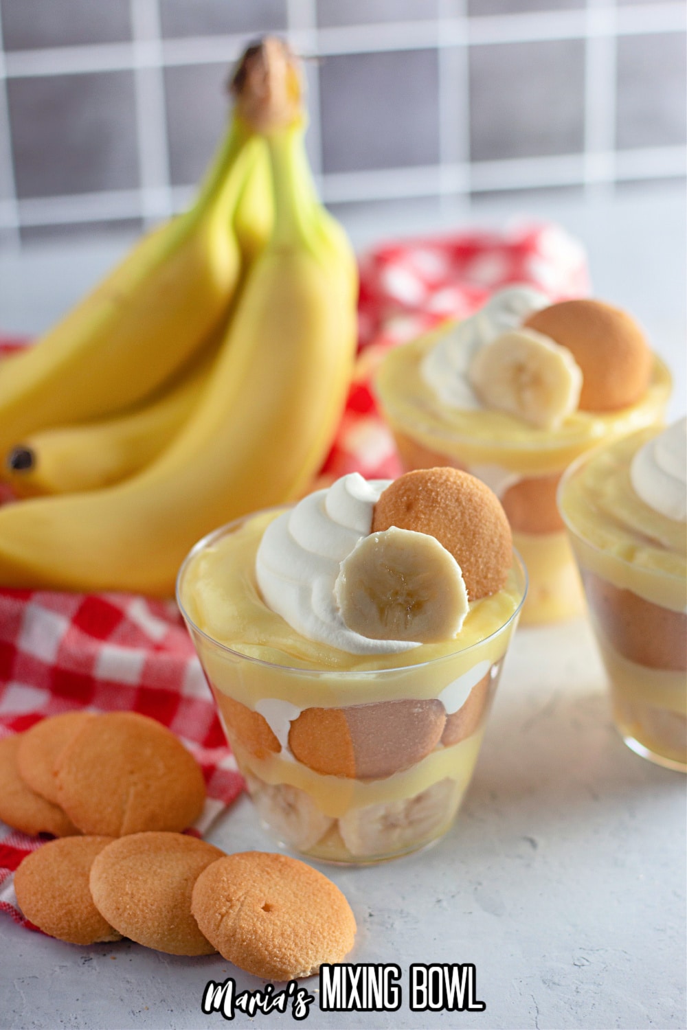 banana pudding in a clear plastic cup with a bunch of bananas in the background