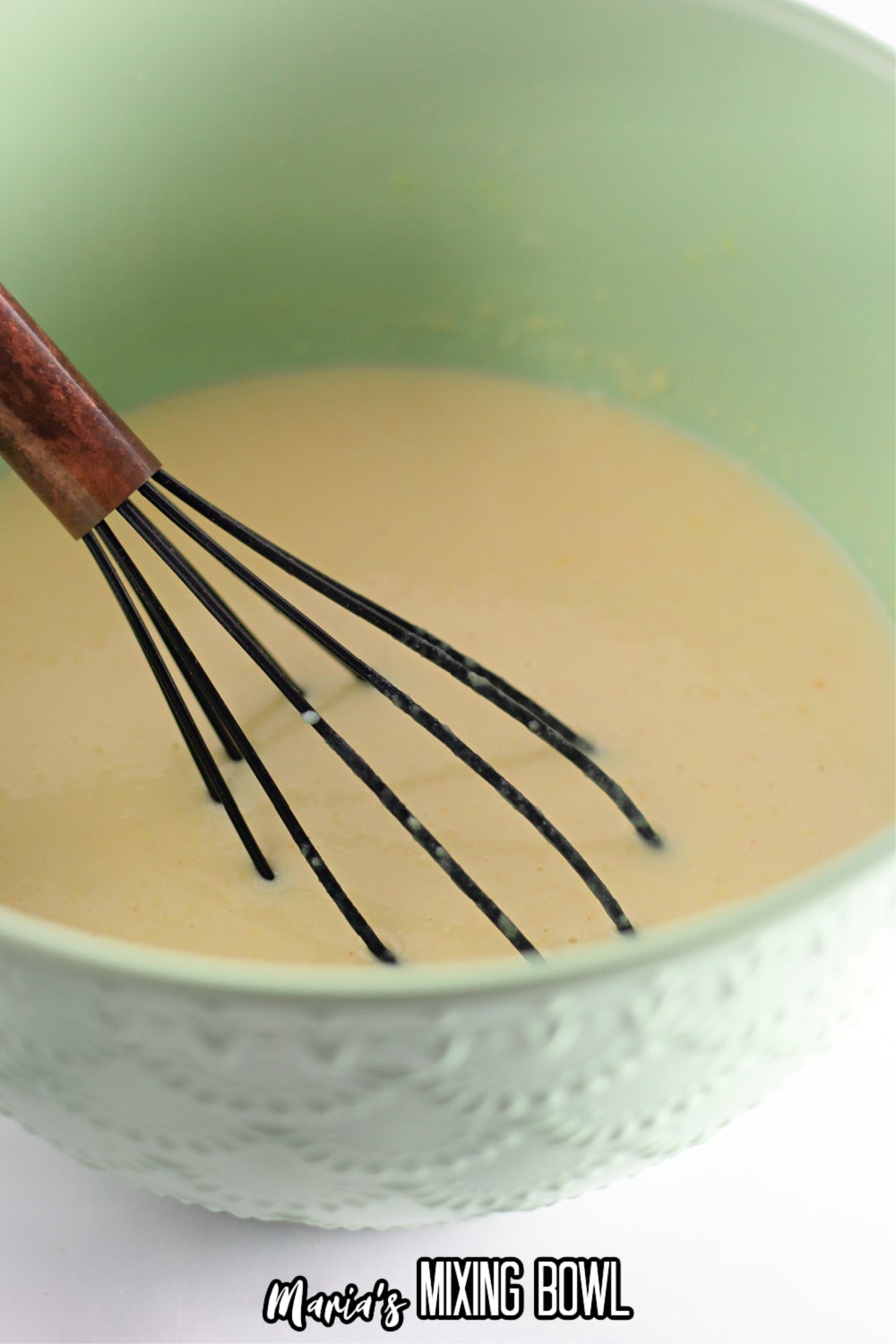vanilla pudding being whisked in a green mixing bowl