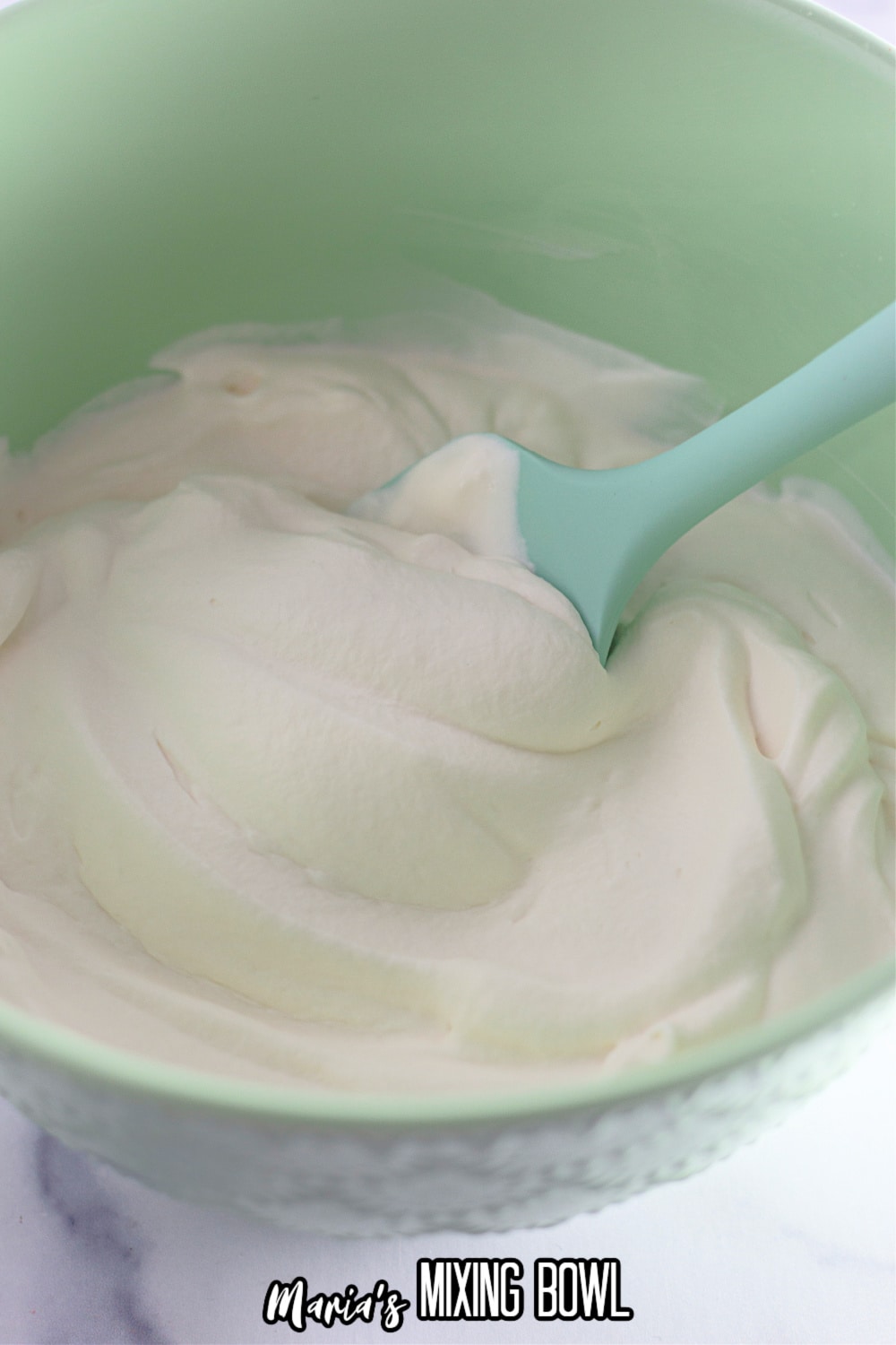 homemade whipped cream in a green mixing bowl being stirred with a green spoon
