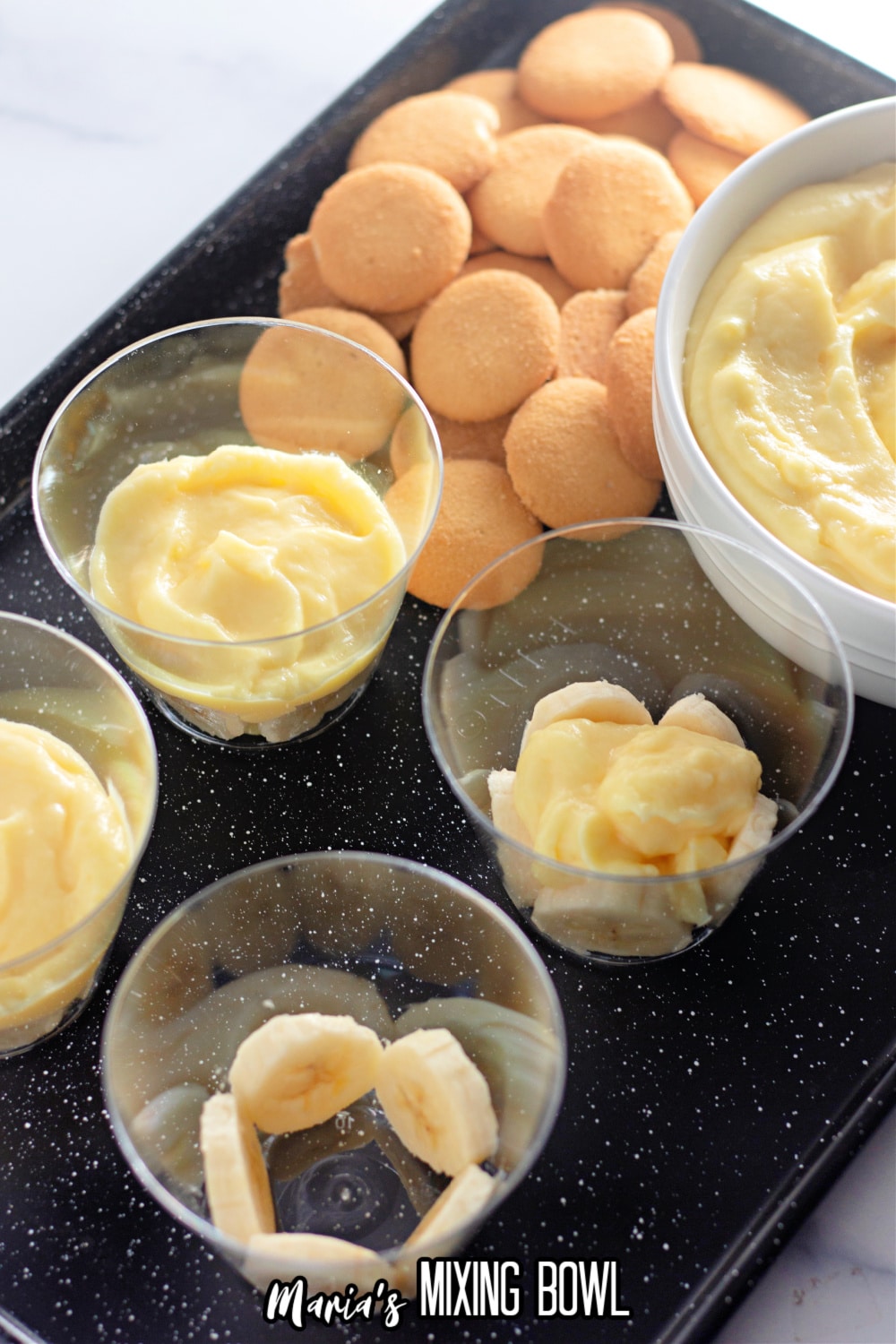 pudding and bananas being layered on a dark baking sheet