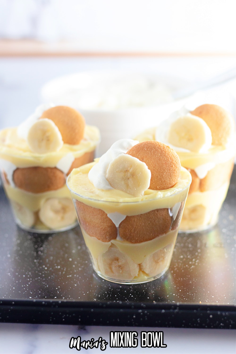 pudding cups being garnished with a slice of banana, a vanilla wafer, and a dollop of whipped cream