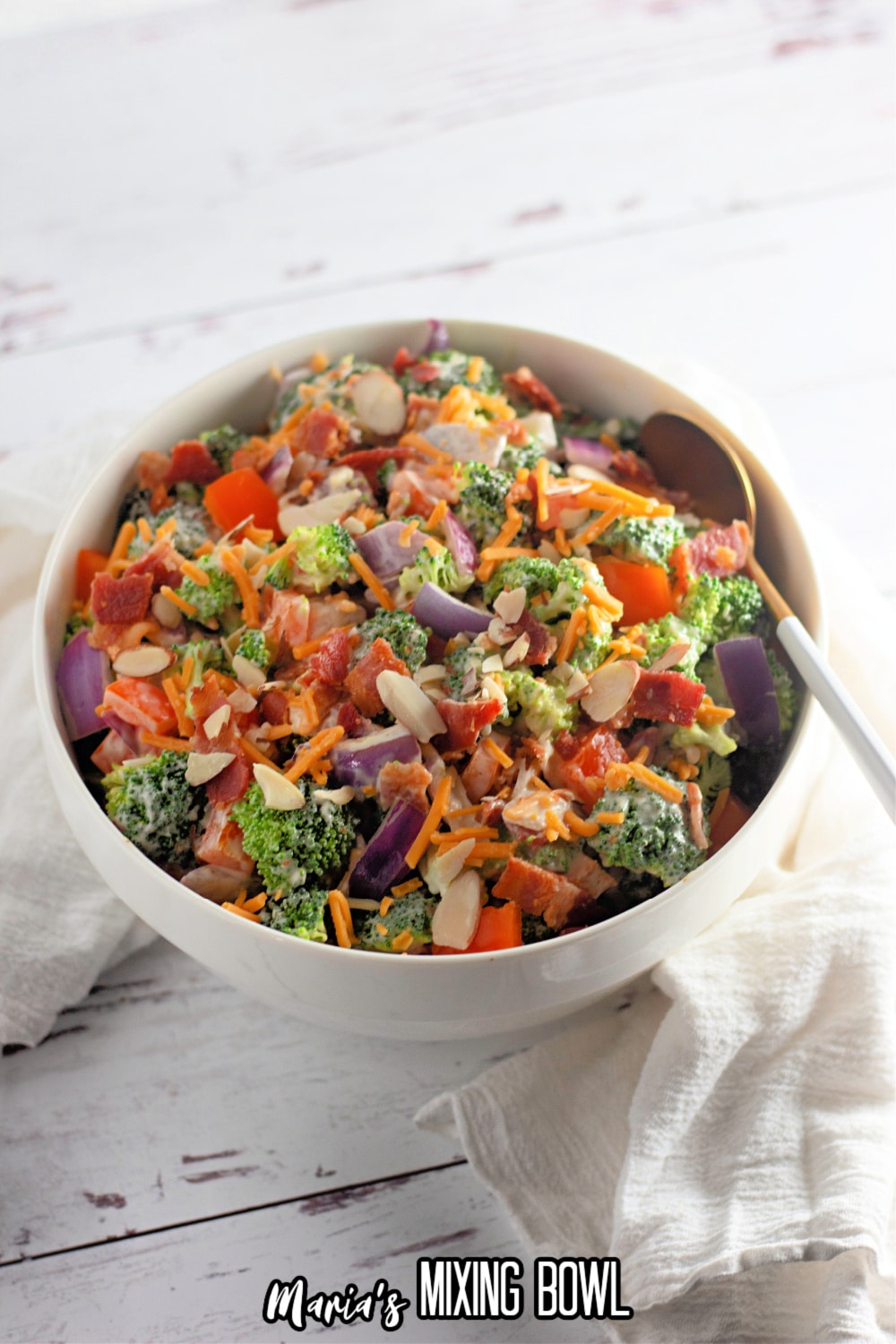broccoli salad in a white bowl with a gold spoon with a white handle