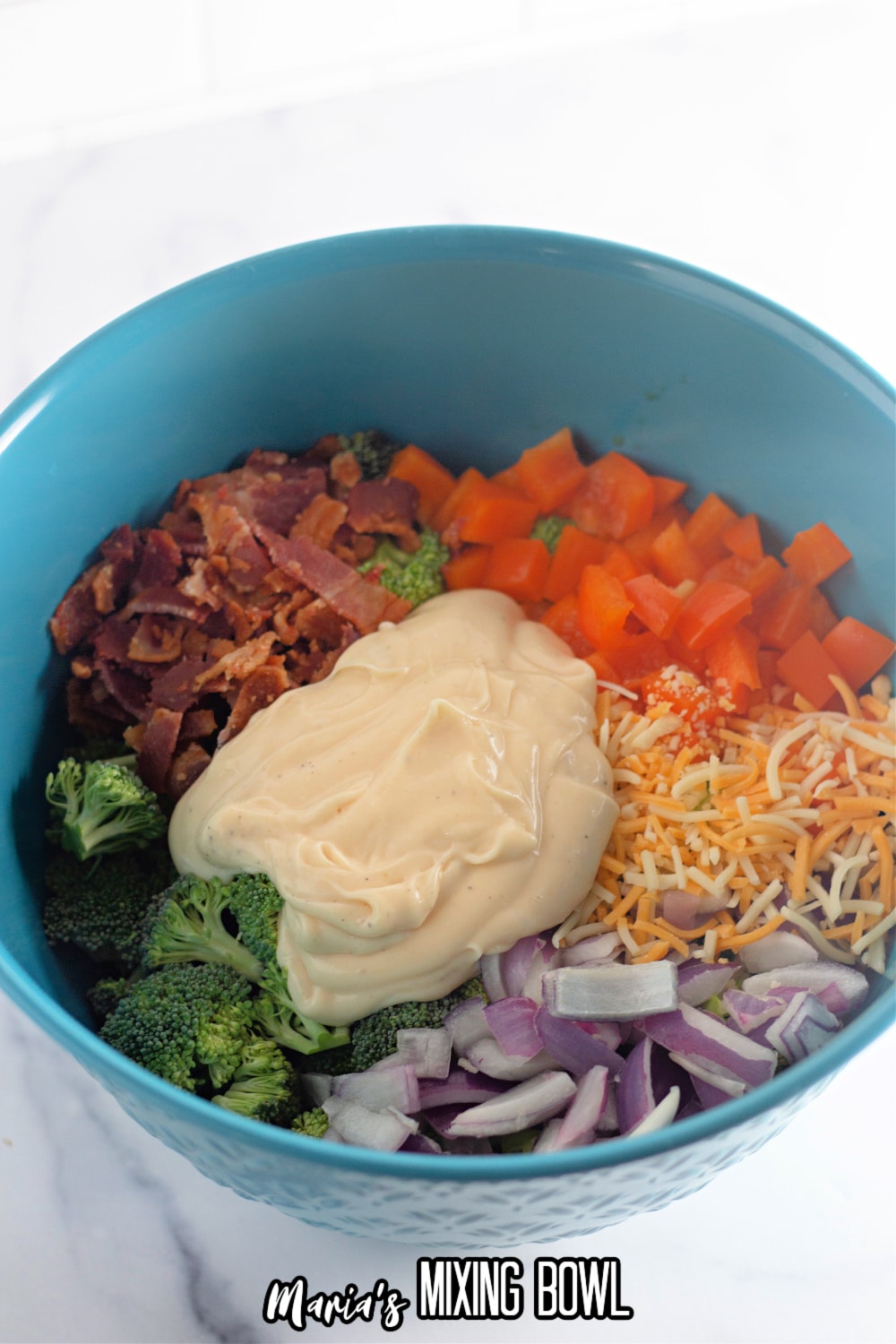 salad dressing being added to a blue bowl of vegetables and bacon