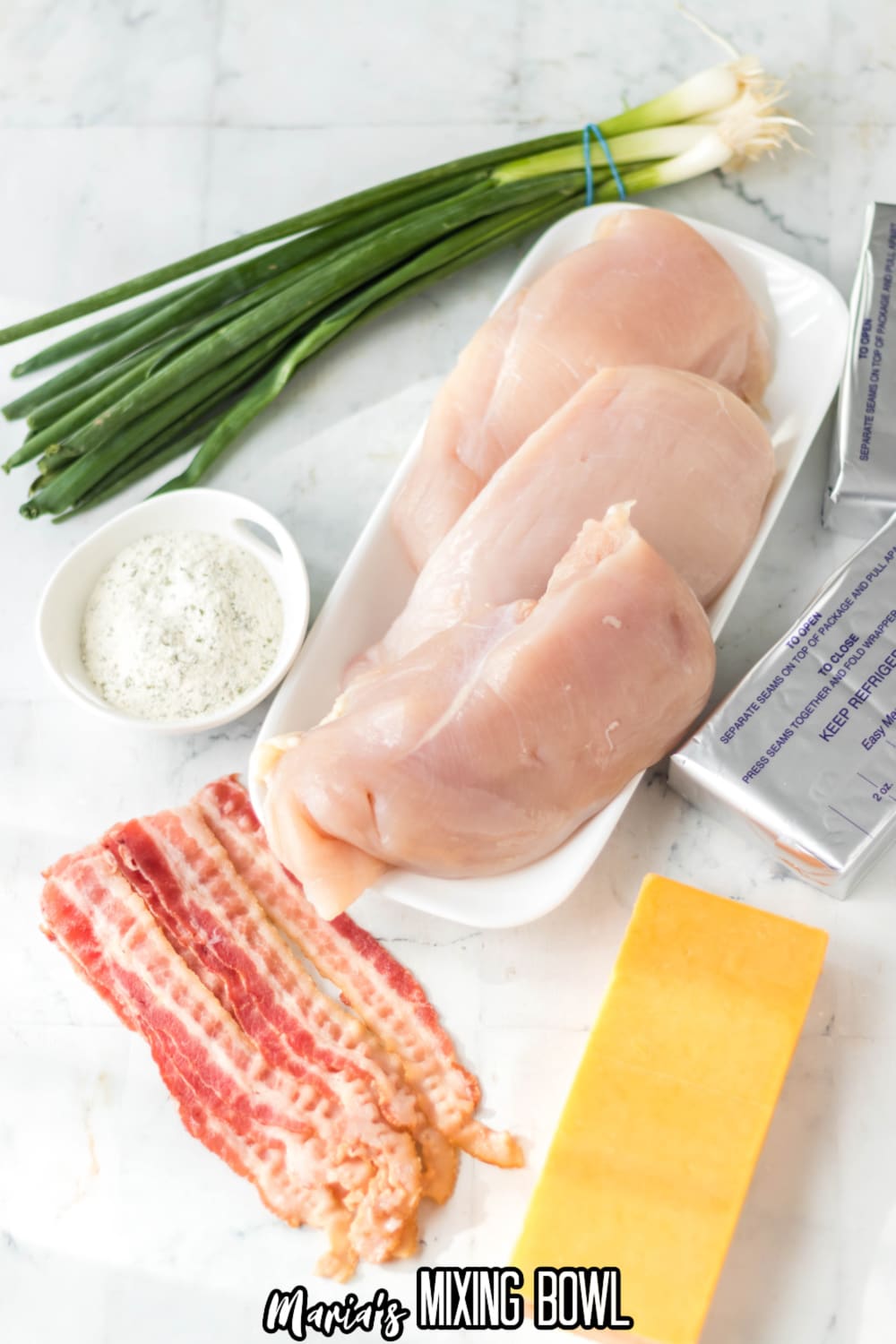 green onions, raw chicken breasts, ranch seasonings, bacon, cheddar cheese, and cream cheese on a white marble background