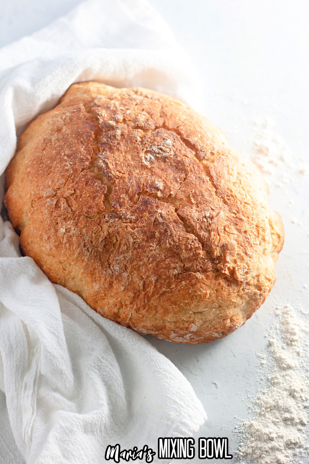 loaf of dutch oven bread on a white background surrounded by a white kitchen towel