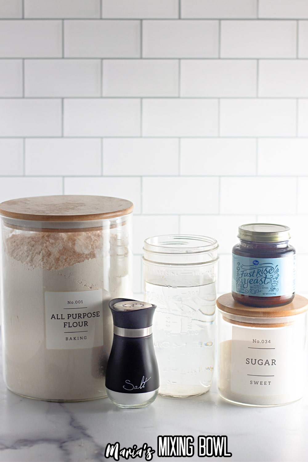 jars of flour, water, yeast, sugar, and a salt shaker on a white marble background