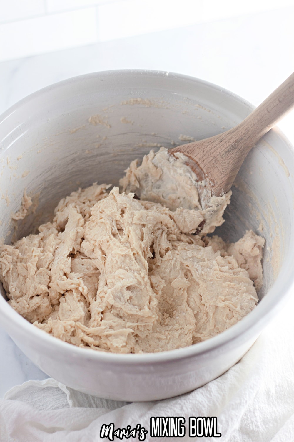 bread dough being mixed with a wooden spoon in a white mixing bowl