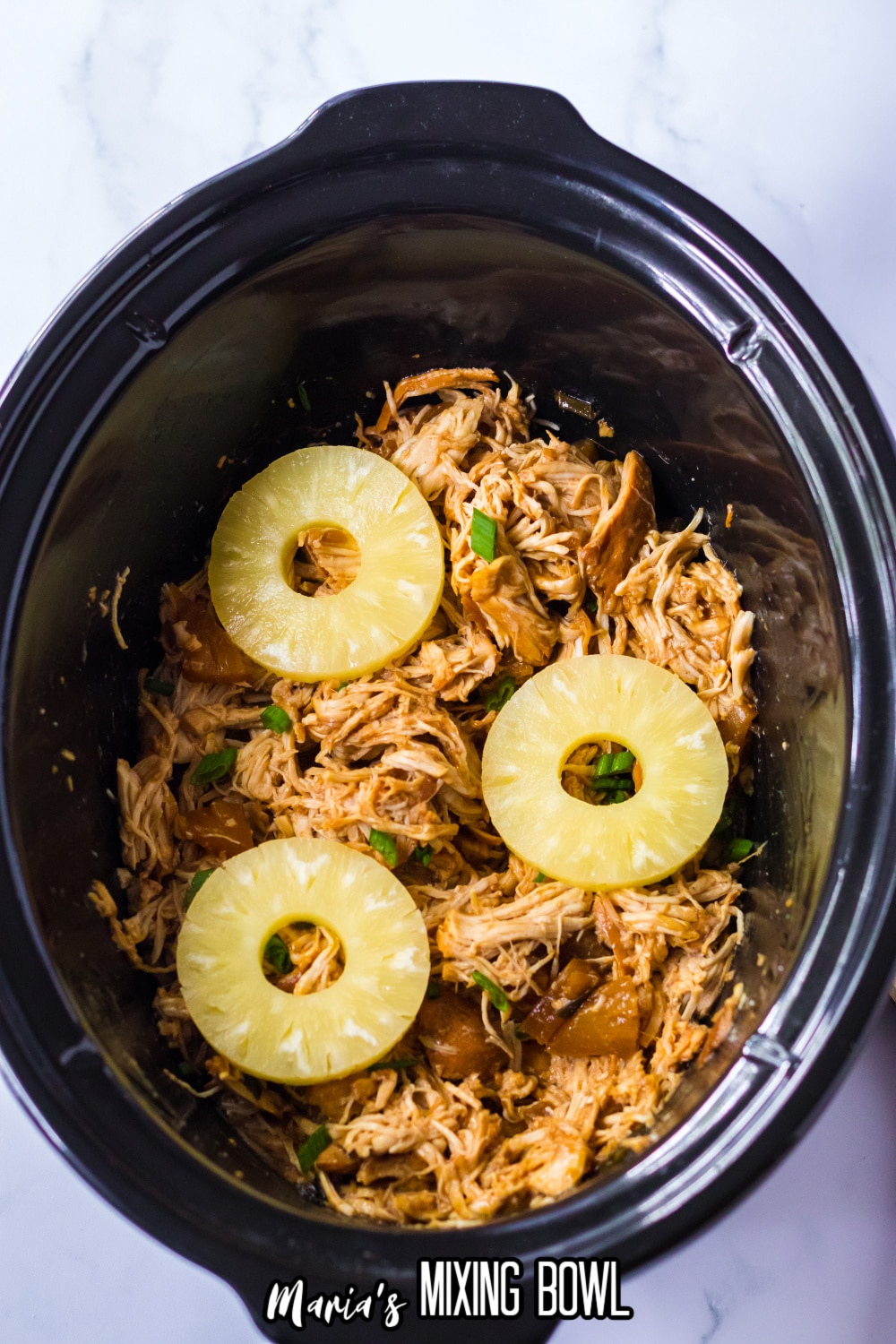 shredded hawaiian chicken topped with pineapple slices in a slow cooker