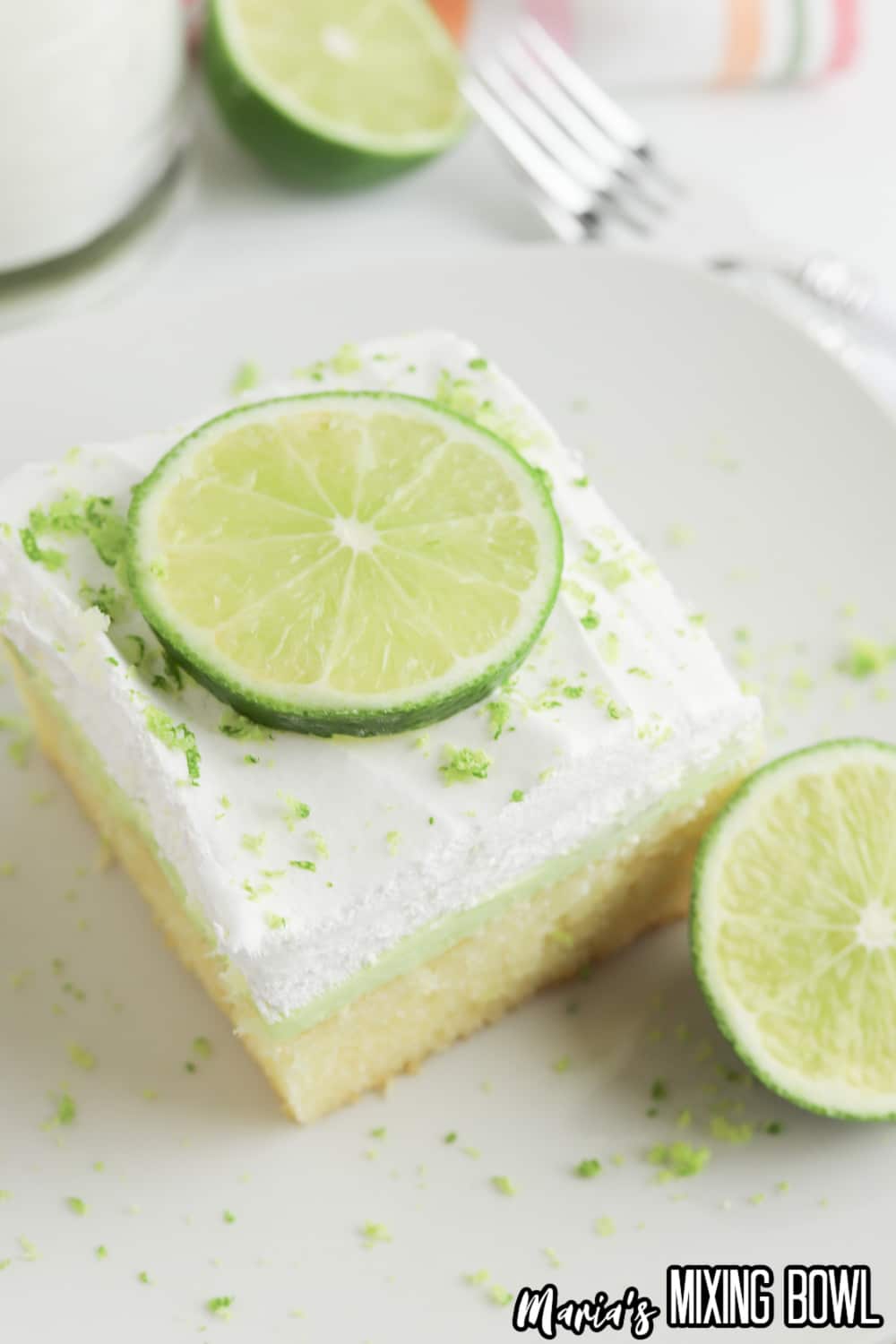 slice of key lime poke cake on a small white plate with a slice of lime on top for garnish