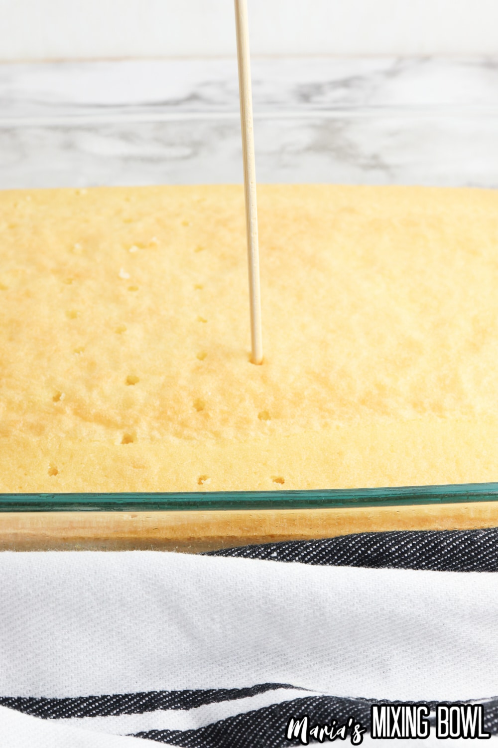 holes being poked in a cake with a wooden skewer