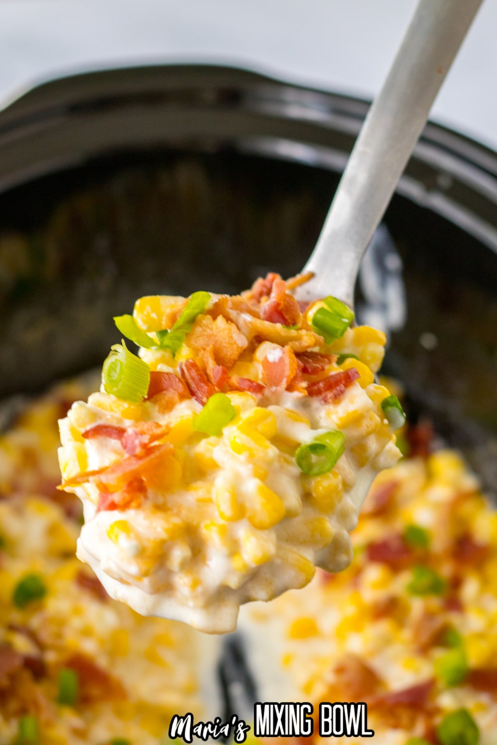 large spoonful of loaded cream corn held in the air above the slow cooker