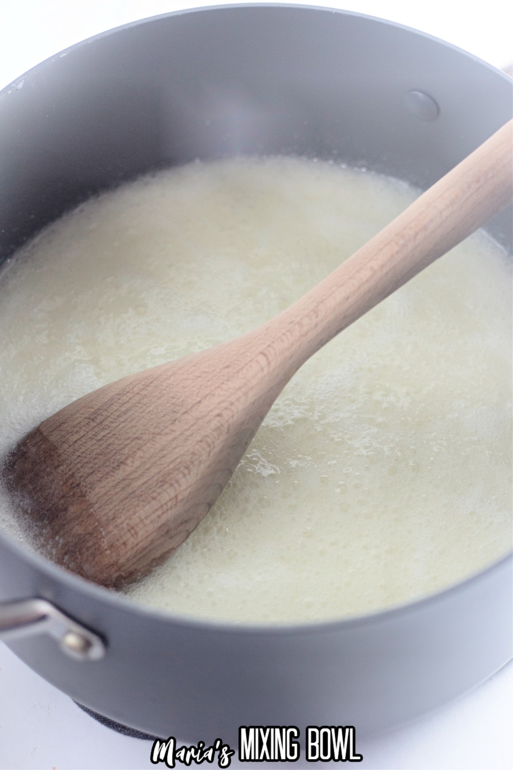 butter, milk and sugar in a stainless steel pot being stirred with a wooden spoon