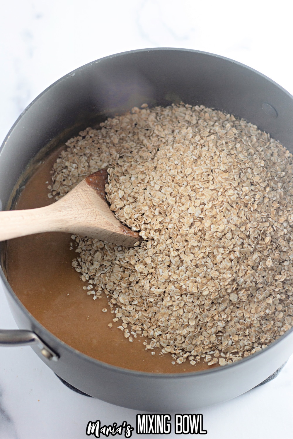 oats being stirred into a melted peanut butter and sugar mixture in a stainless steel pot