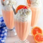 three milkshake glasses filled with orange cream shakes topped with whipped cream, cherries, and orange slices