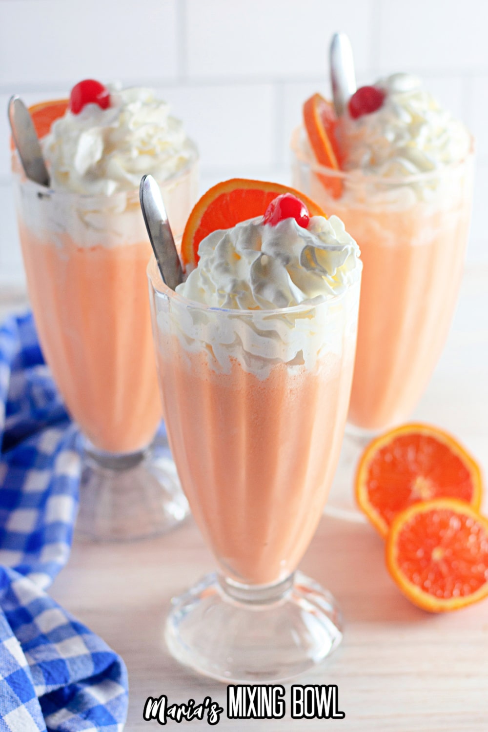 three milkshake glasses filled with orange cream shakes topped with whipped cream, cherries, and orange slices