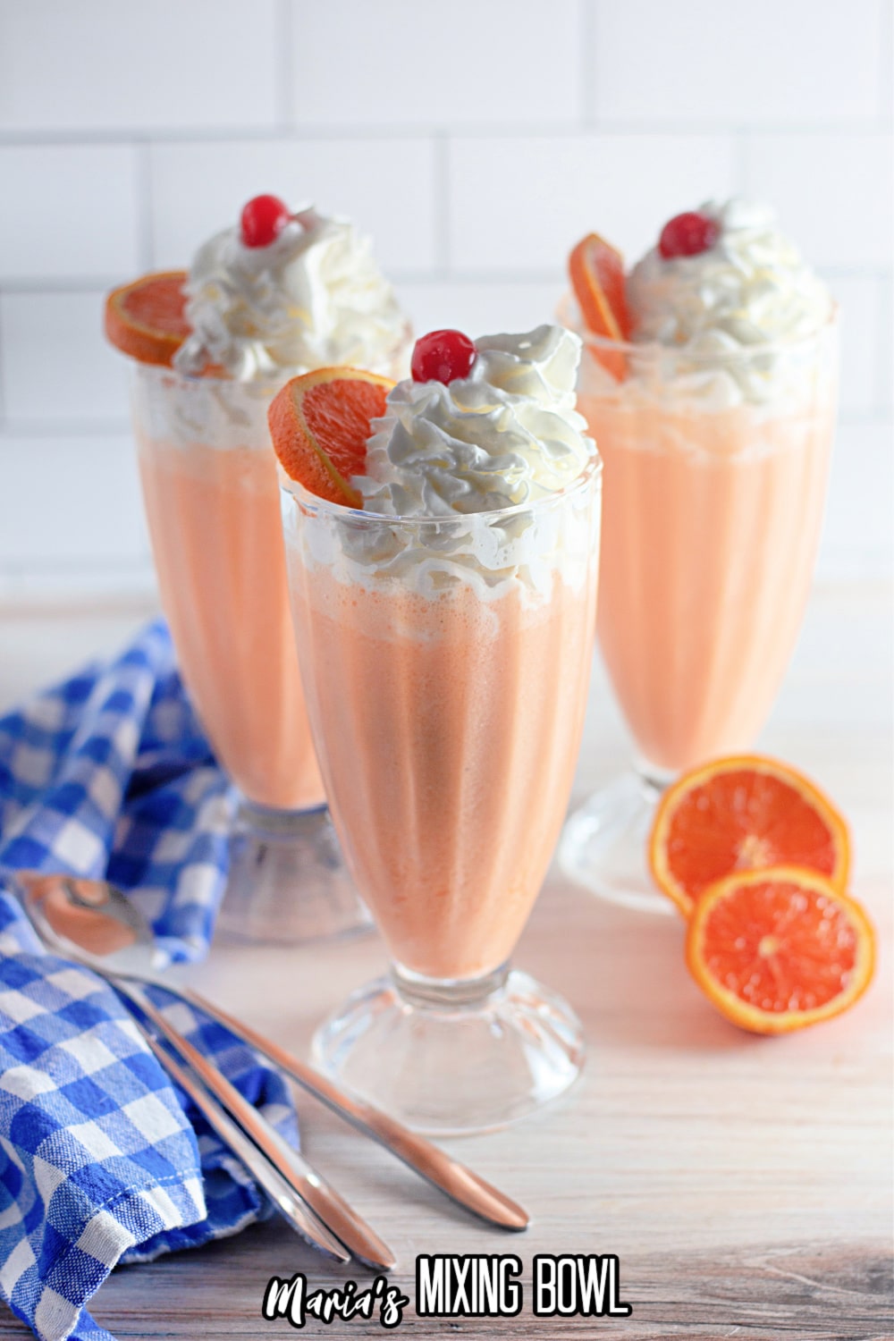 three milkshake glasses filled with orange cream shakes topped with whipped cream, cherries, and orange slices