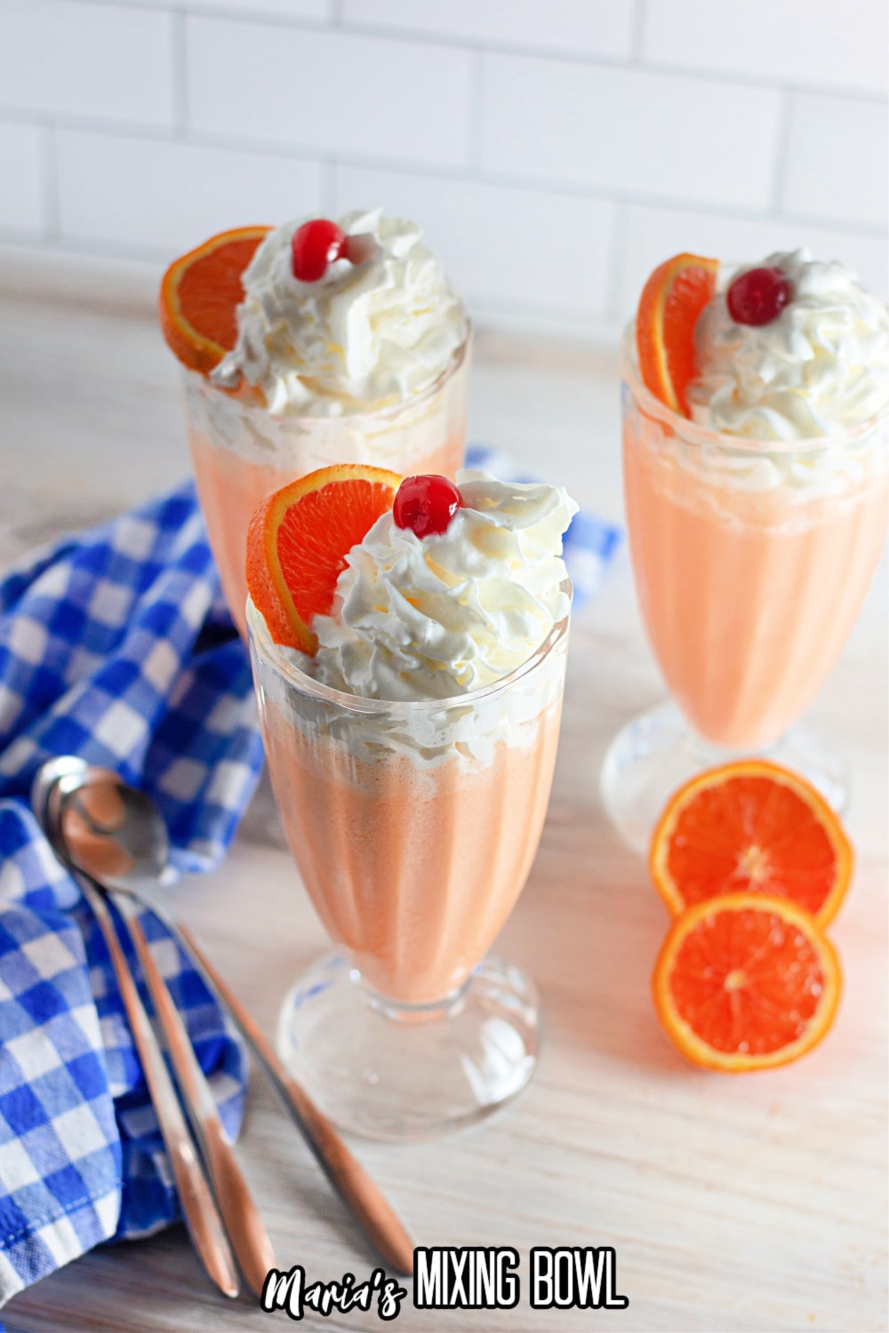 three milkshake glasses filled with orange cream shakes topped with whipped cream, cherries, and orange slices