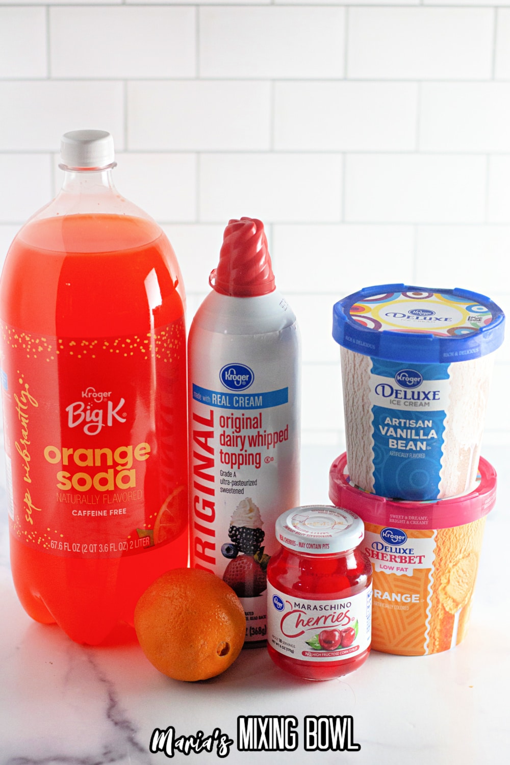 bottle of orange soda, whipped cream, an orange, jar of cherries, vanilla ice crema, and orange sherbet