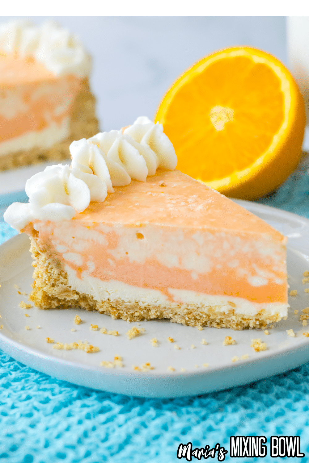 slice of orange cheesecake on a white plate on top of a bright blue kitchen towel