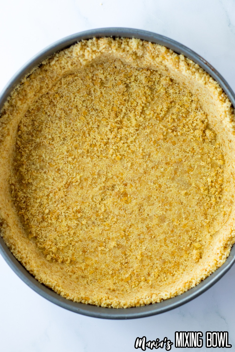 graham cracker crust being pressed into the bottom and sides of a sprinform pan