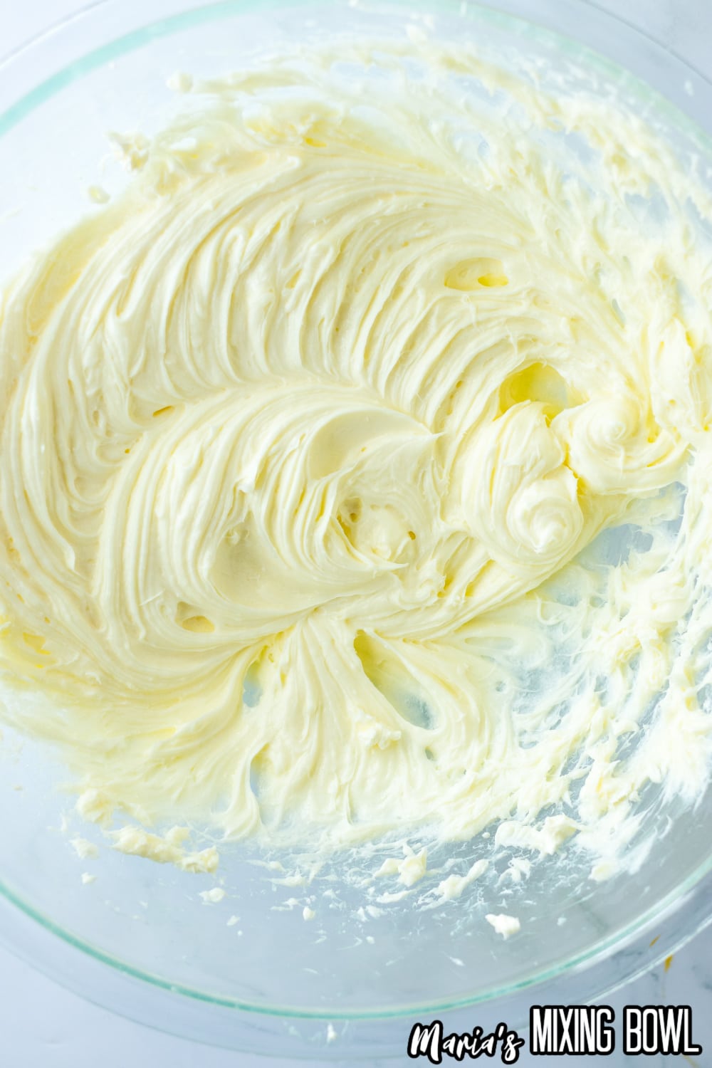 cream cheese and sugar being creamed together in a glass mixing bowl