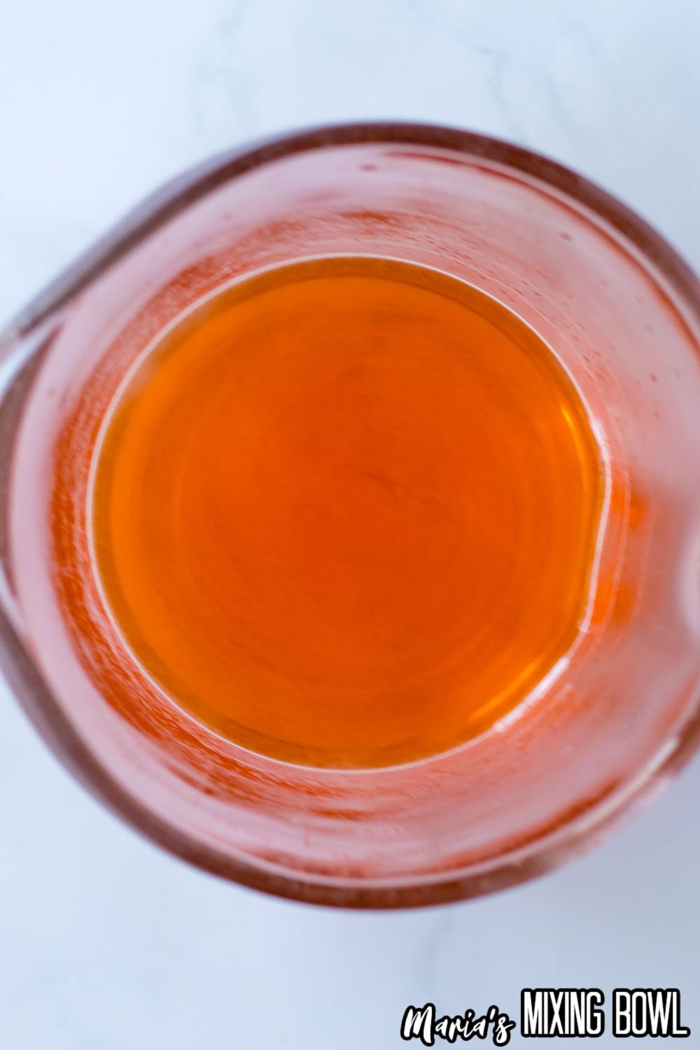 orange gelatin being mixed with water in a glass mixing cup