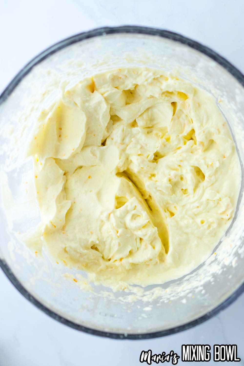 whipped cream being mixed in a glass mixing bowl