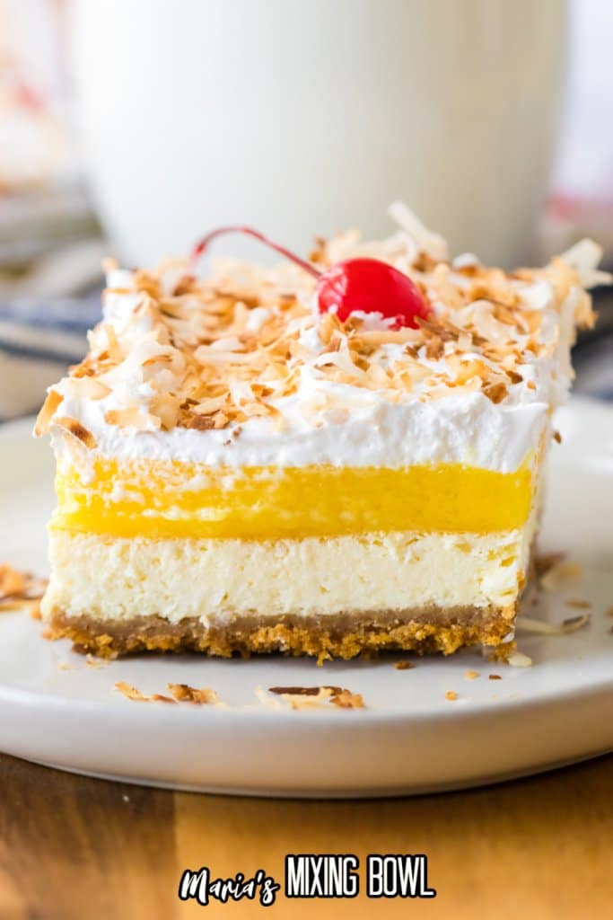slice of pina colada cheesecake bar topped with toasted coconut and cherries on a white plate