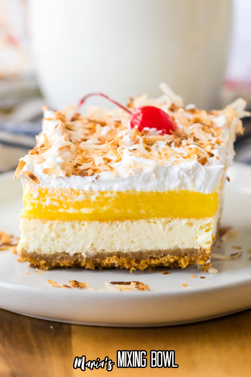 slice of pina colada cheesecake bar topped with toasted coconut and cherries on a white plate