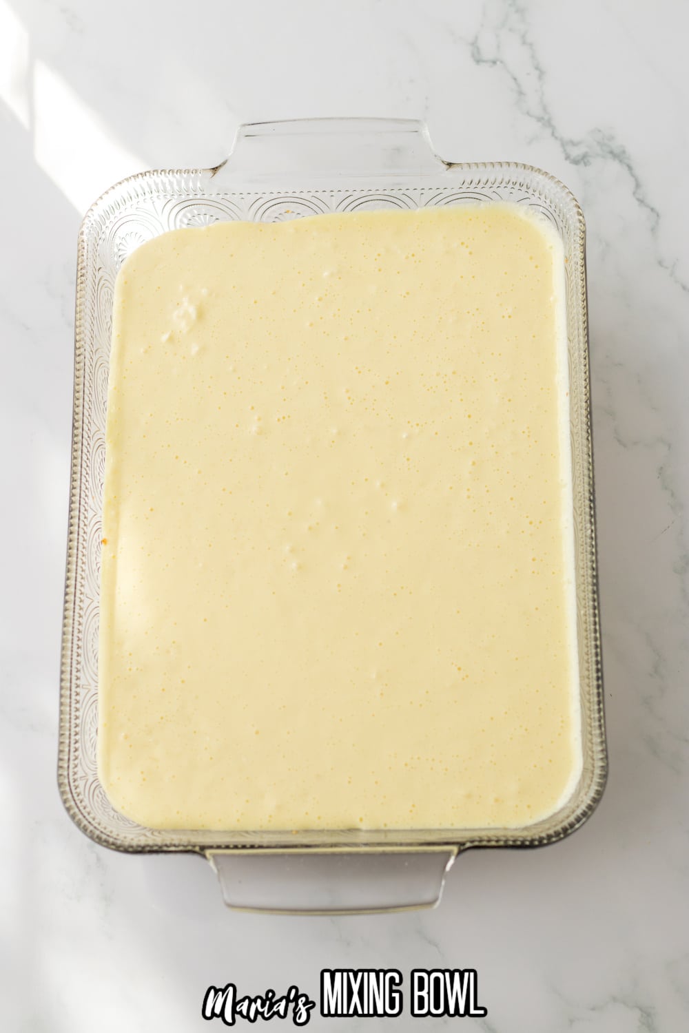 cream cheese layer being spread on top of a graham cracker crust in a glass baking dish