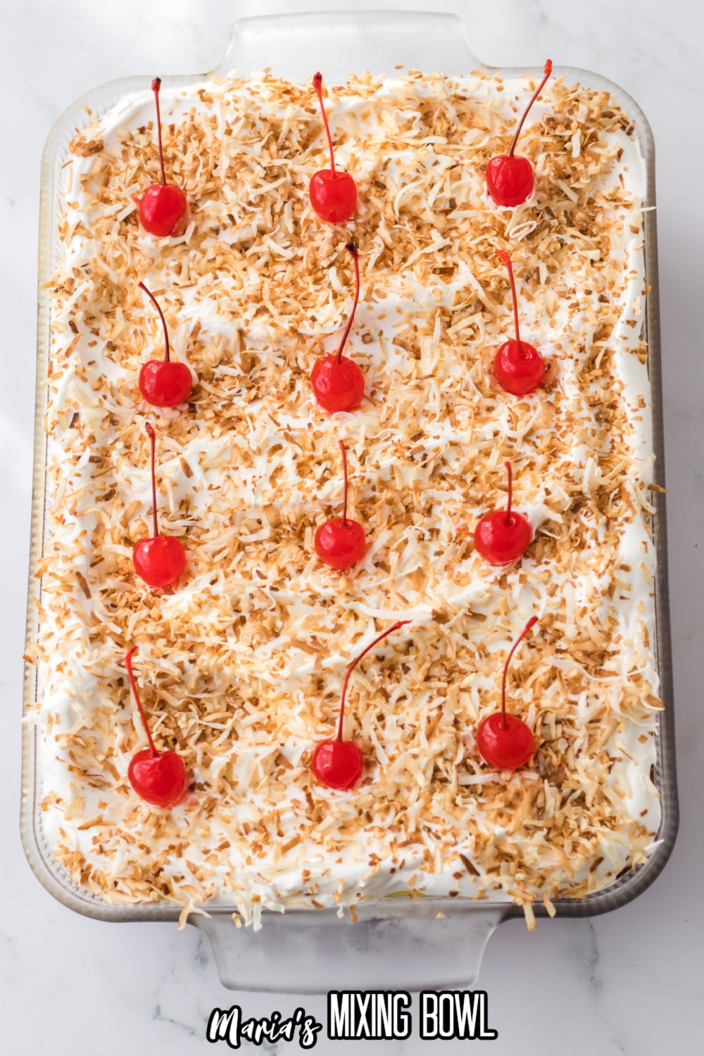 cherries and toasted coconut being placed on top of a finished dessert in a glass baking dish