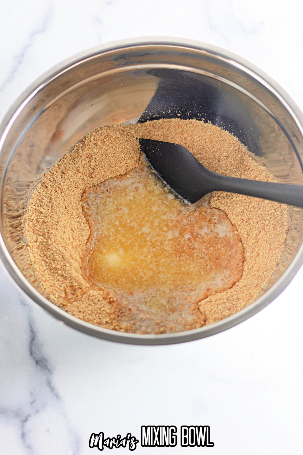graham cracker crumbs in a stainless steal mixing bowl being mixed with melted butter