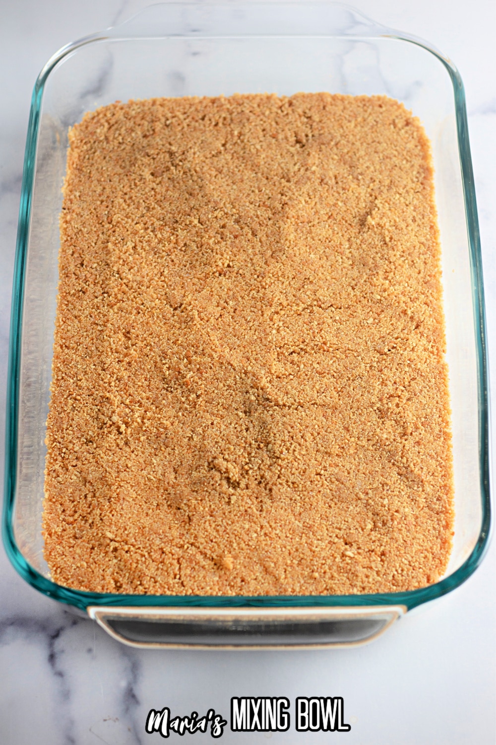 graham cracker crust being pressed into a glass baking dish