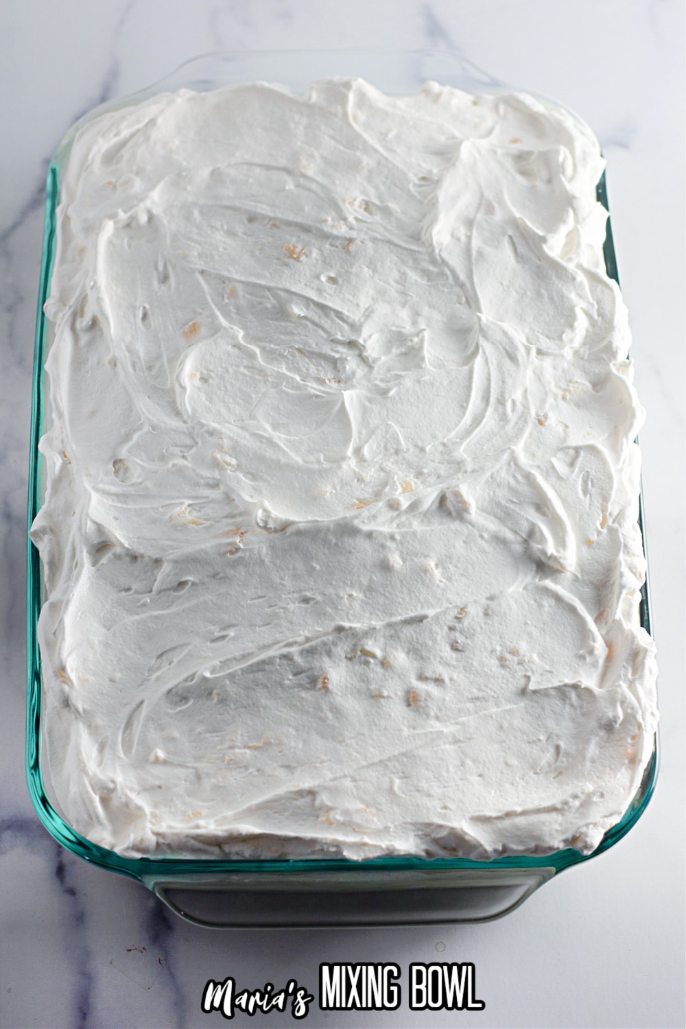 pineapple whipped being spread on top of a dessert in a glass baking dish