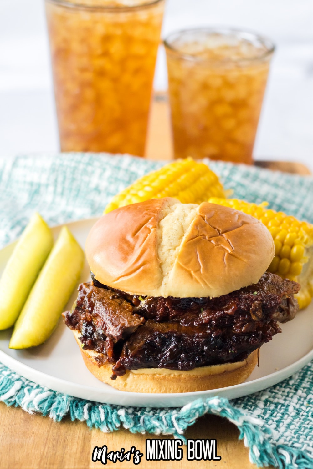 sliced beef brisket on a white plate with two mini corn cobs and two slices of pickle