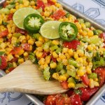 finished spicy corn salad in a metal tray with slices of limes and jalapenos on the top