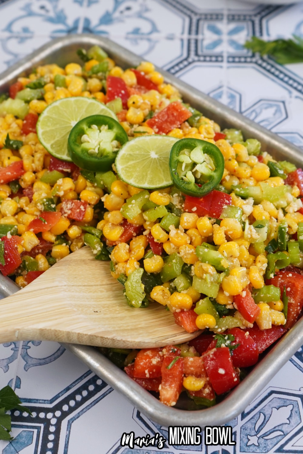 finished spicy corn salad in a metal tray with slices of limes and jalapenos on the top