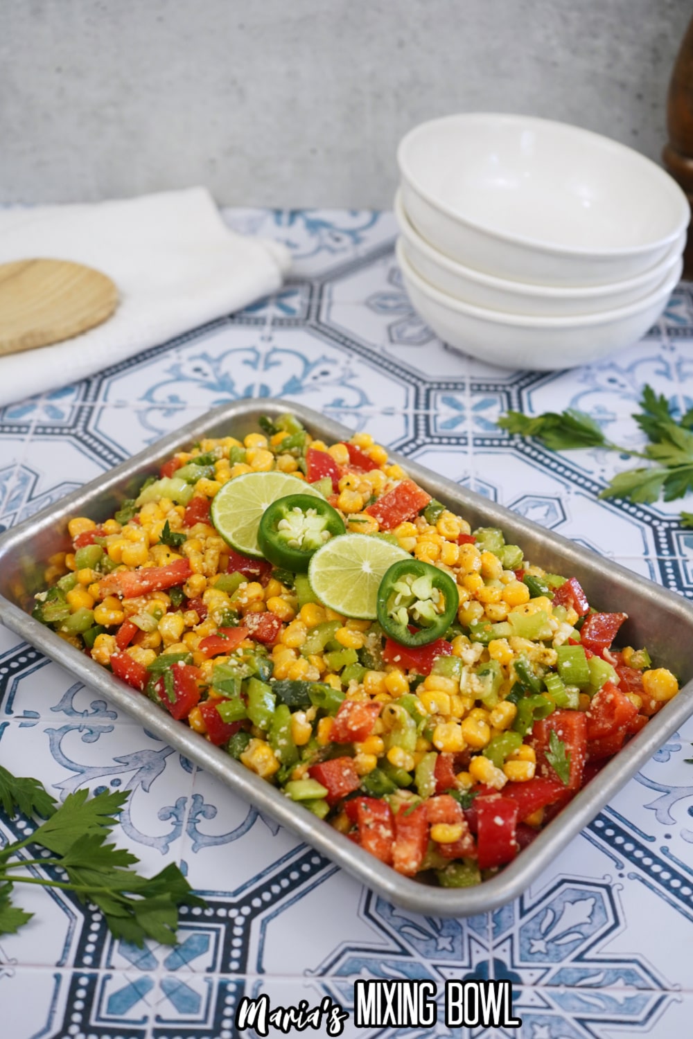 finished spicy corn salad in a metal tray with slices of limes and jalapenos on the top