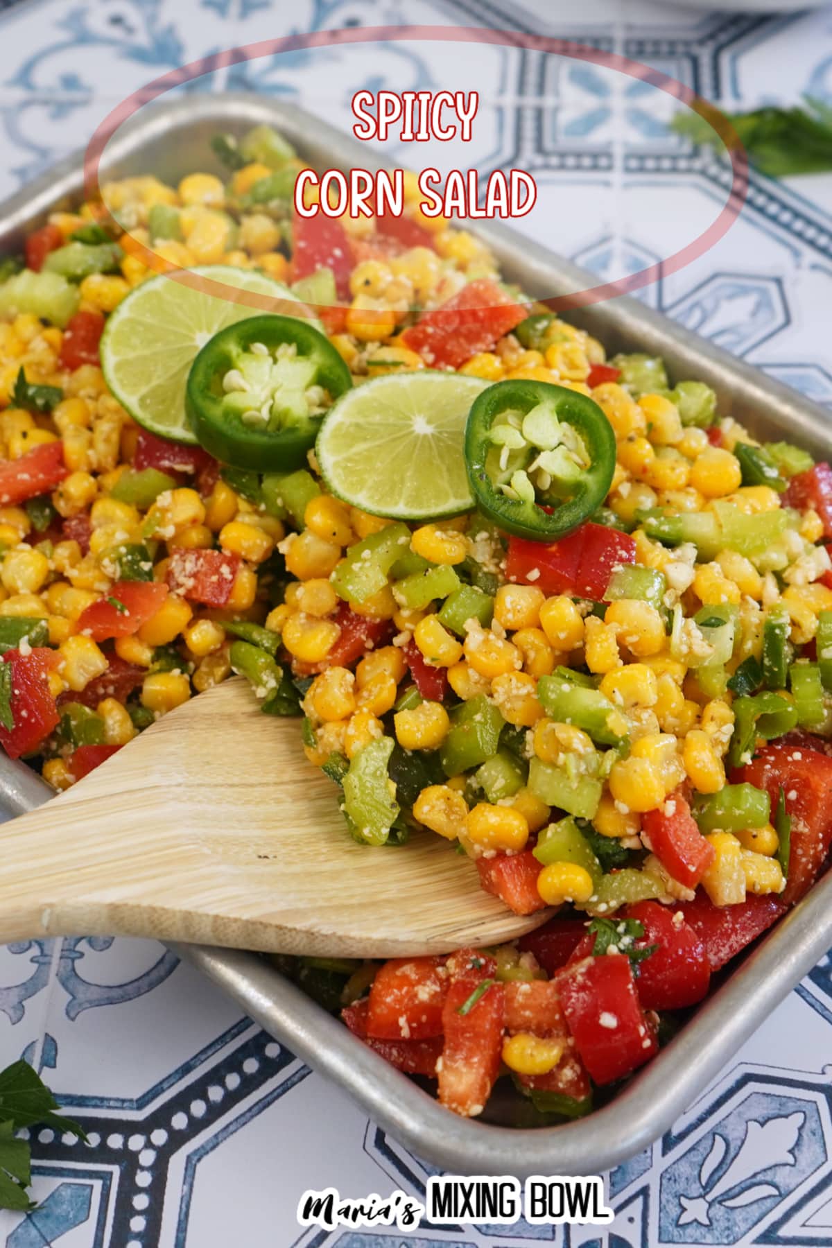 finished spicy corn salad in a metal tray with slices of limes and jalapenos on the top