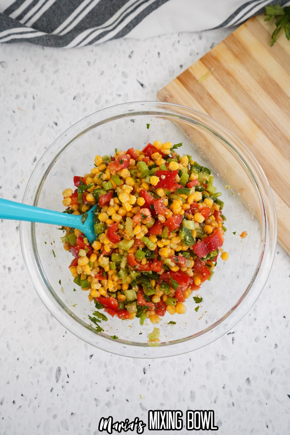 corn salad being mixed with a rubber spatula in a glass mixing bowl