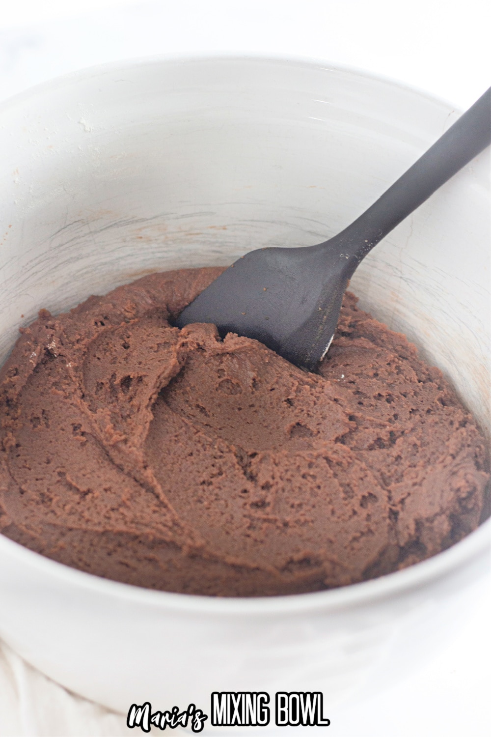 chocolate cookie dough in a white mixing bowl being stirred with a rubber spatula