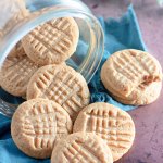 peanut butter cookies being spilled out of a glass jar on a wooden board