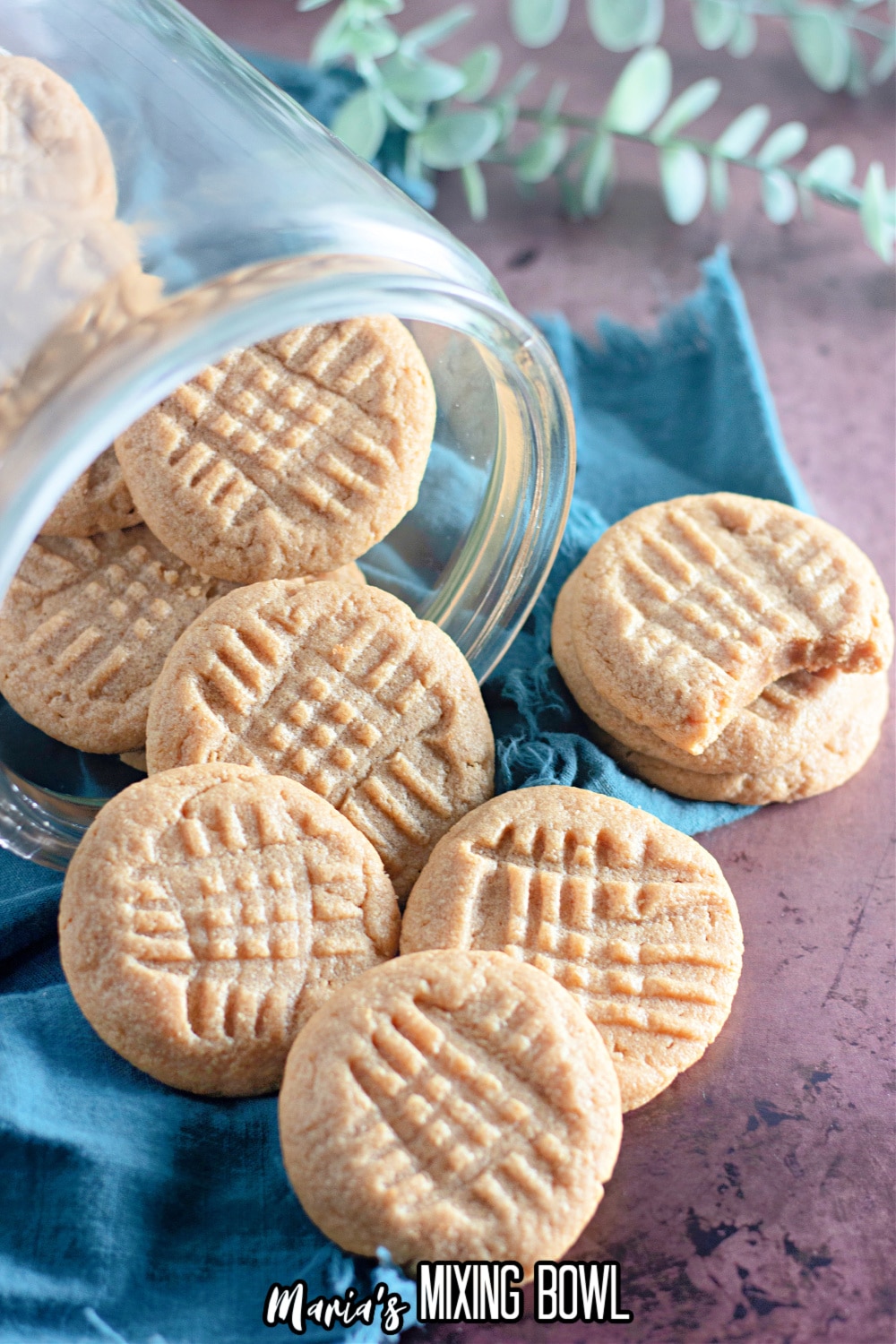 peanut butter cookies being spilled out of a glass jar on a wooden board