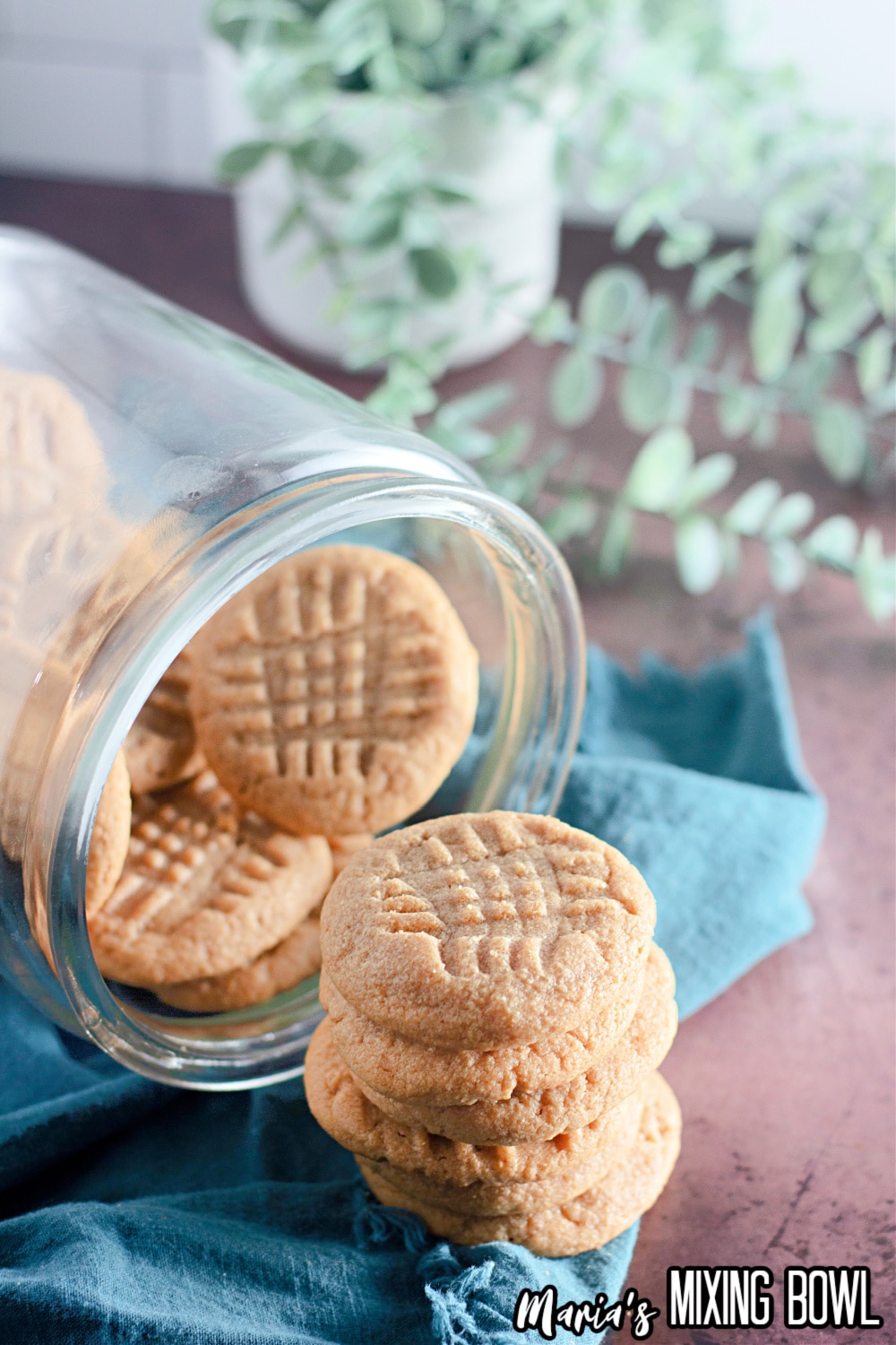 peanut butter cookies being spilled out of a glass jar on a wooden board