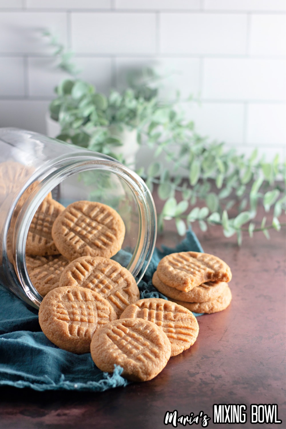 peanut butter cookies being spilled out of a glass jar on a wooden board