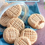 peanut butter cookies being spilled out of a glass jar on a wooden board