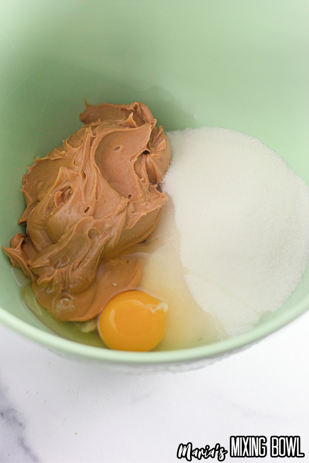 peanut butter, sugar, and egg in a green mixing bowl