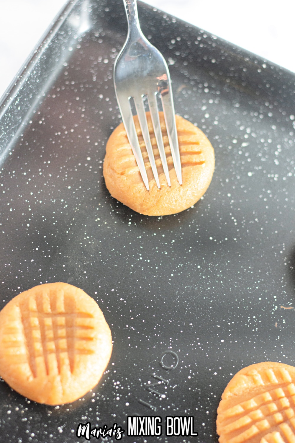 peanut butter cookie on a baking sheet being scored with a fork